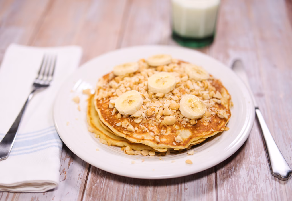 A stack of golden macadamia nut pancakes topped with toasted macadamia nuts and bananas